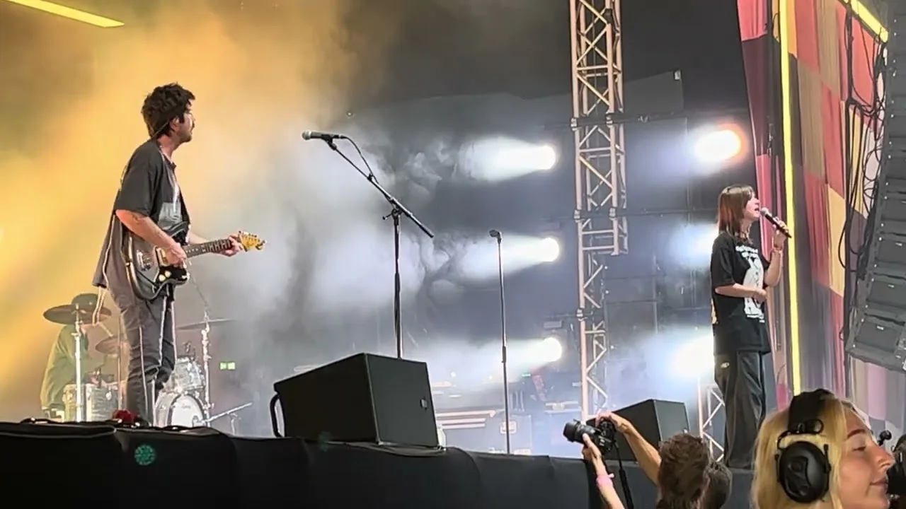 Ethel Cain and her guitarist on a wide festival stage in daylight haze, photographers crouched in the pit below. Roskilde Festival, Denmark · July 2023. Frame from footage by tonyagren, © the uploader.