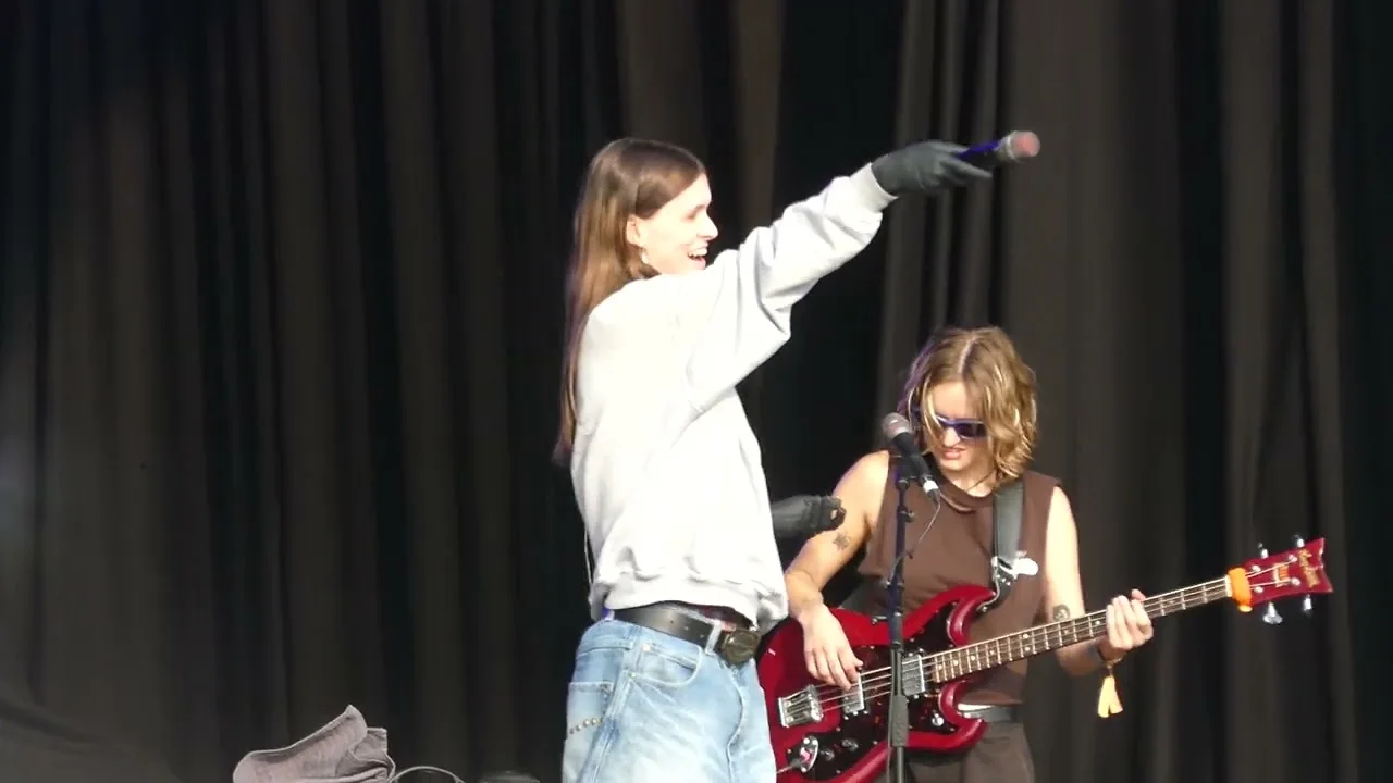 Ethel Cain with her arm raised beside her guitarist, the festival stage open behind them. All Points East, Victoria Park, London · 18 August 2024. Frame from footage by GotsomePearlJam, © the uploader.