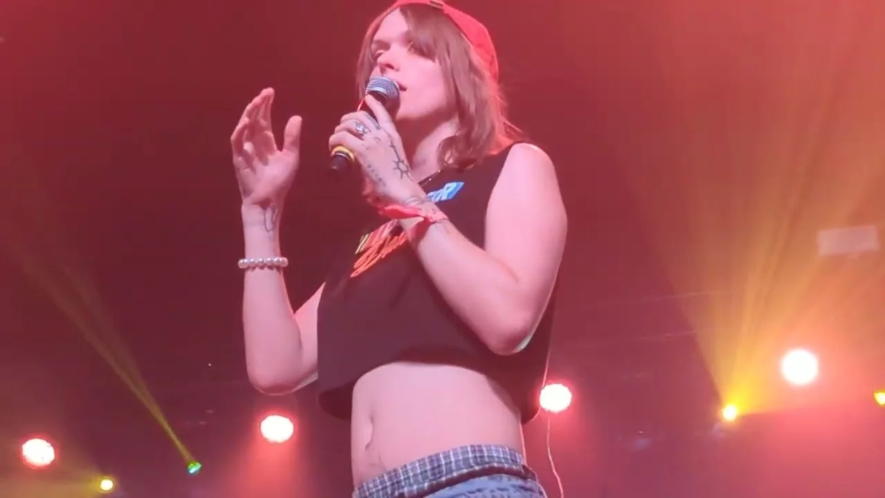 Ethel Cain in a black crop top under warm stage light at Coachella, one hand lifted mid-line. Coachella, Indio · 23 April 2023. Frame from footage by Brooks Marshall, © the uploader.